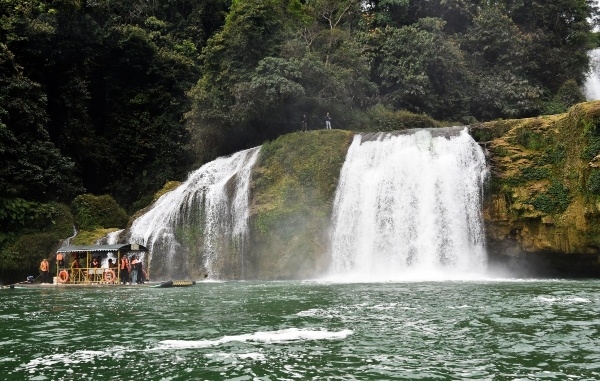游客们坐在船上观赏瀑布落在归春河上。
